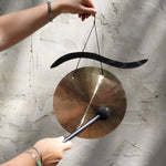 Someone holding the Woodstock Hand-Hammered Brass Hanging Gong in front of a white wall.