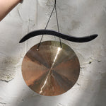 Someone holding the Woodstock Hand-Hammered Brass Hanging Gong in front of a white wall.