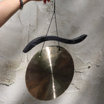 Someone holding the Woodstock Hand-Hammered Brass Hanging Gong in front of a white wall.