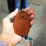 An up-close image of someone holding the wooden clapper from the Woodstock Dahlia Garden Wind Chime in front of a cement wall.