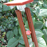 Someone holding the Medium Turquoise Woodstock Wind Chime in front of a green bush.