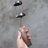 Someone holding the bottom of the Copper Quintet Woodstock Temple Bells Wind Chime in front of a concrete wall.
