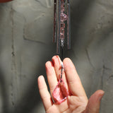 Someone holding the Rose Gem Drop Wind Chime in front of a white cement wall.