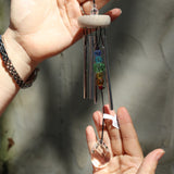 Someone holding the Prism Gem Drop Wind Chime in front of a white cement wall.