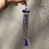 Someone holding the Sapphire Gem Drop Wind Chime in front of a white cement wall.