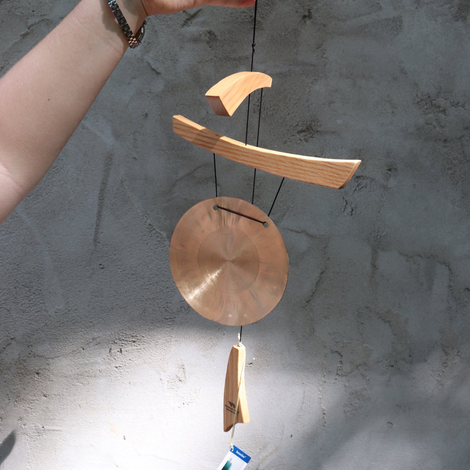 Someone holding the Small Emperor Gong Wind Chime in front of a white wall.
