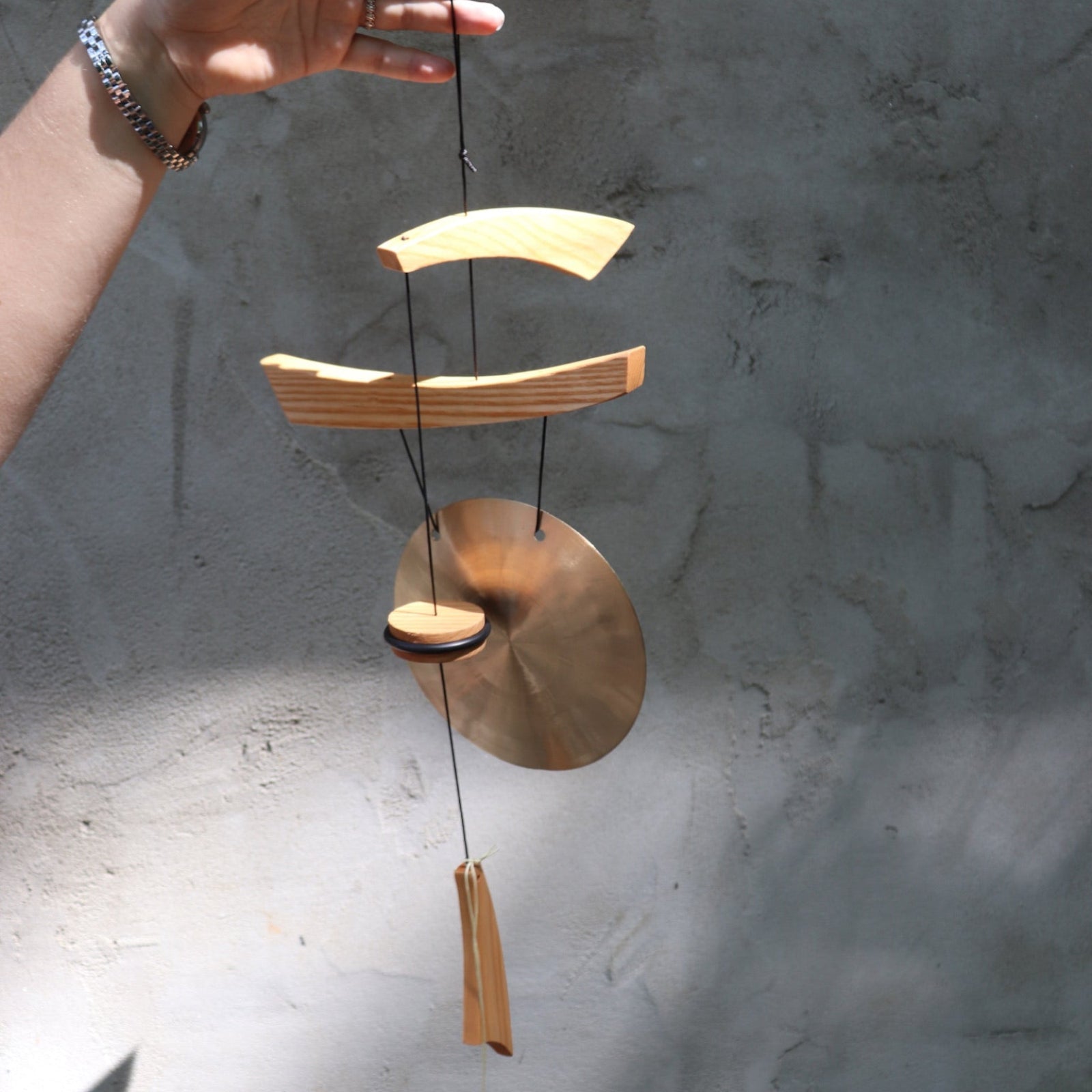 Someone holding the Small Emperor Gong Wind Chime in front of a white wall.