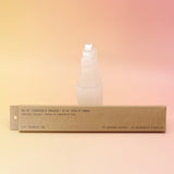 The P.F. Candle Co. Teakwood & Tobacco Incense in front of a selenite tower all on a pink and yellow background.