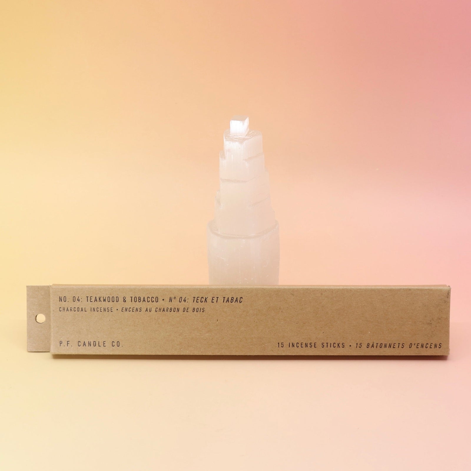 The P.F. Candle Co. Teakwood & Tobacco Incense in front of a selenite tower all on a pink and yellow background.