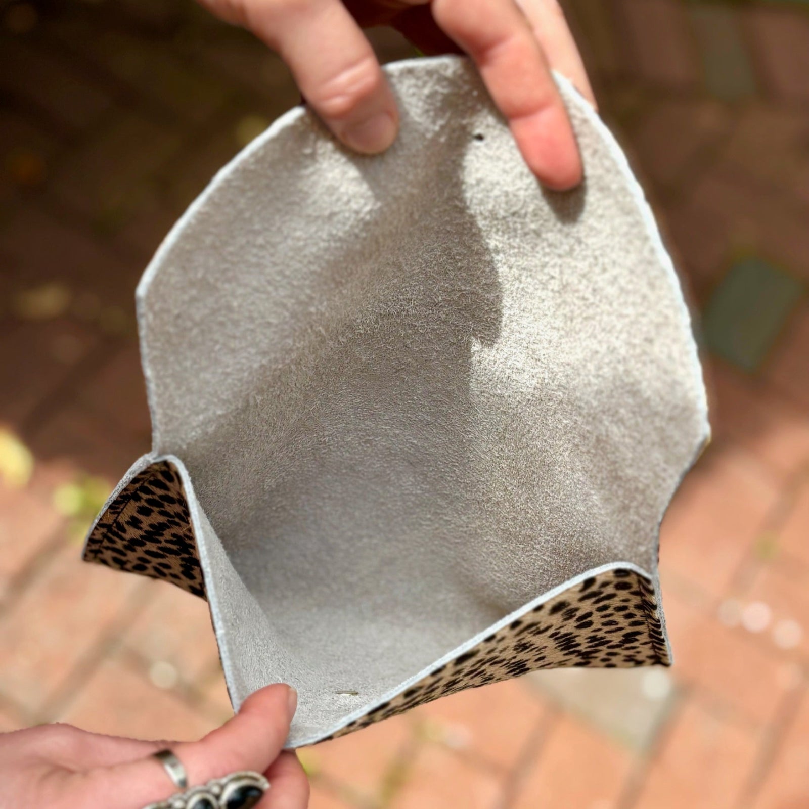 Someone holding the Tiny Spotted Hair on Hide Envelope Pouch Clutch open to show the inside.