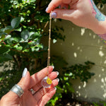 The Taurus Zodiac Car Charm Suncatcher being held in front of a cream-colored brick wall with greenery.