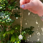 The Aries Zodiac Car Charm Suncatcher being held in front of a cream-colored brick wall with greenery.