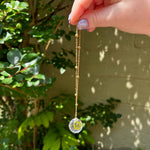 The Scorpio Zodiac Car Charm Suncatcher being held in front of a cream-colored brick wall with greenery.