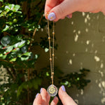 The Cancer Zodiac Car Charm Suncatcher being held in front of a cream-colored brick wall with greenery.