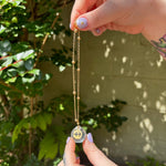 The Sagittarius Zodiac Car Charm Suncatcher being held in front of a cream-colored brick wall with greenery.
