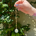 The Pisces Zodiac Car Charm Suncatcher being held in front of a cream-colored brick wall with greenery.
