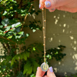 The Gemini Zodiac Car Charm Suncatcher being held in front of a cream-colored brick wall with greenery.