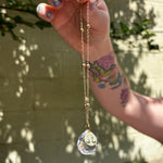 The Scorpio Zodiac Car Charm Suncatcher being held in front of a cream-colored brick wall with greenery.