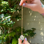 The Virgo Zodiac Car Charm Suncatcher being held in front of a cream-colored brick wall with greenery.