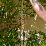 Someone holding the Amazonite Lotus Crystal Suncatcher in front of a cream-colored brick wall with greenery.