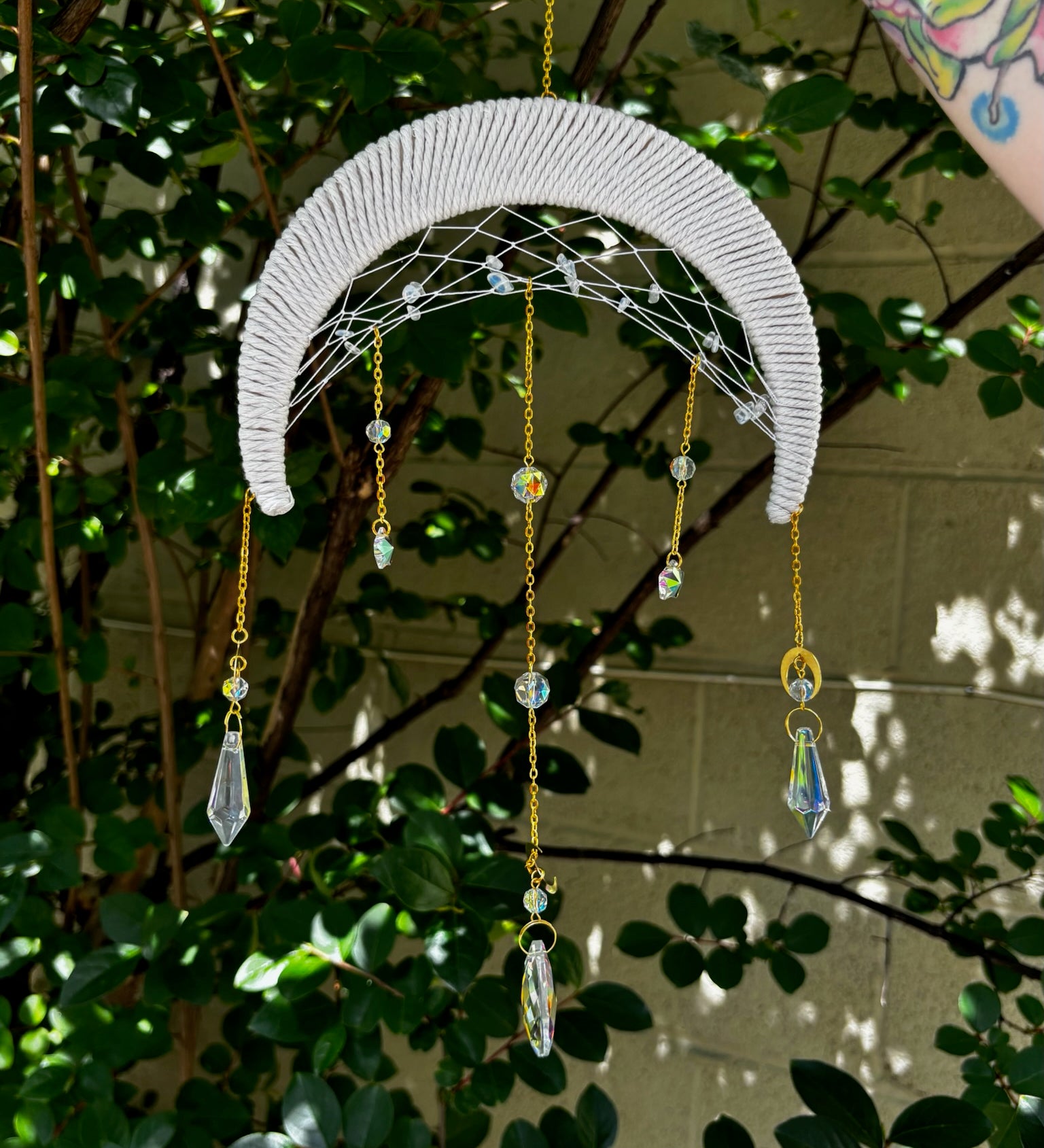 The Fantasy Opalite Suncatcher in front of a white wall with greenery behind it.