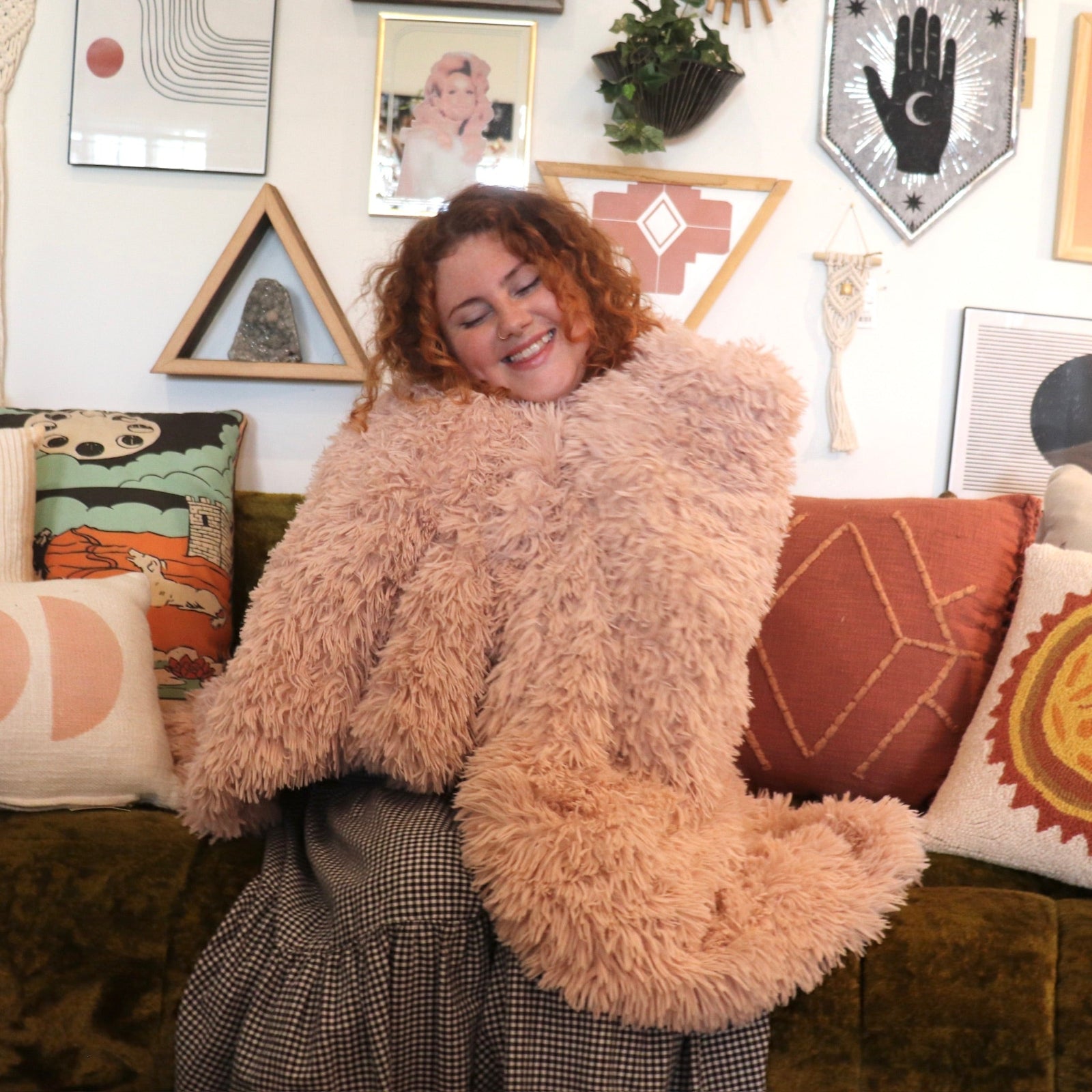A woman on a couch wrapped in the Pink Hero Dreamy Faux Fur Throw Blanket.