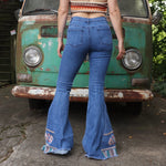 A woman wearing the Midtone Embroidered Denim Bell Bottoms and a red, orange, and brown crochet top in front of a vintage Volkswagen bus.