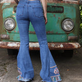 A woman wearing the Midtone Embroidered Denim Bell Bottoms in front of a vintage Volkswagen bus.