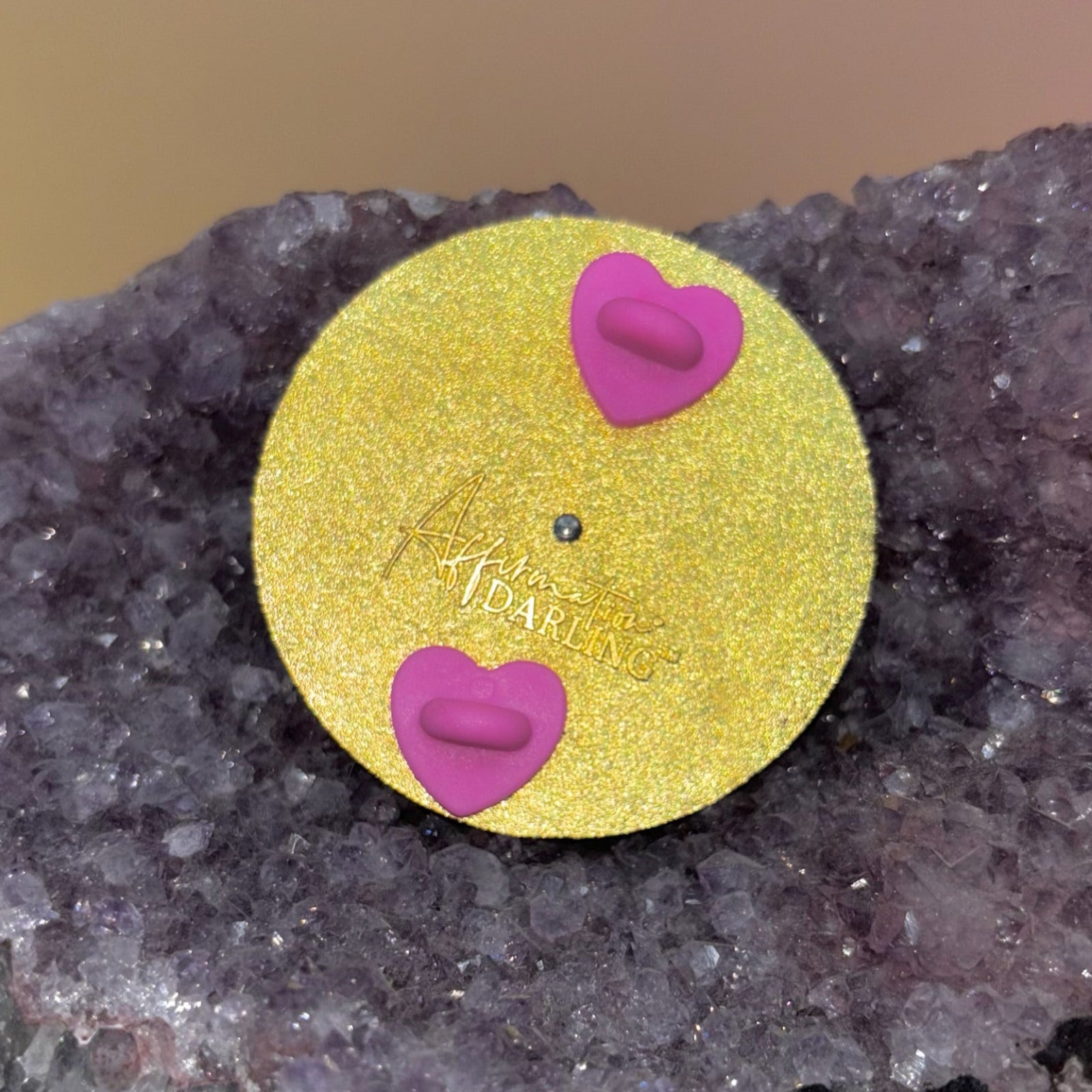 The back of the Word for Today Enamel Pin on an amethyst piece all on a pink and yellow background.