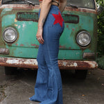 A woman wearing the Western Red Suede Stars Flared Denim Jeans with a red, orange, and brown top all in front of a vintage Volkswagen van.