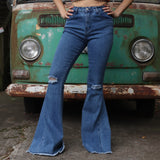 A woman wearing the Western Midtone Ripped and Fringed Stretchy Flared Jeans with a red, orange, and brown top all in front of a vintage Volkswagen bus.