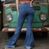 A woman wearing the Western Midtone Ripped and Fringed Stretchy Flared Jeans with a red, orange, and brown top all in front of a vintage Volkswagen bus.