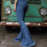 A woman wearing the Western Midtone Ripped and Fringed Stretchy Flared Jeans with a red, orange, and brown top all in front of a vintage Volkswagen bus.