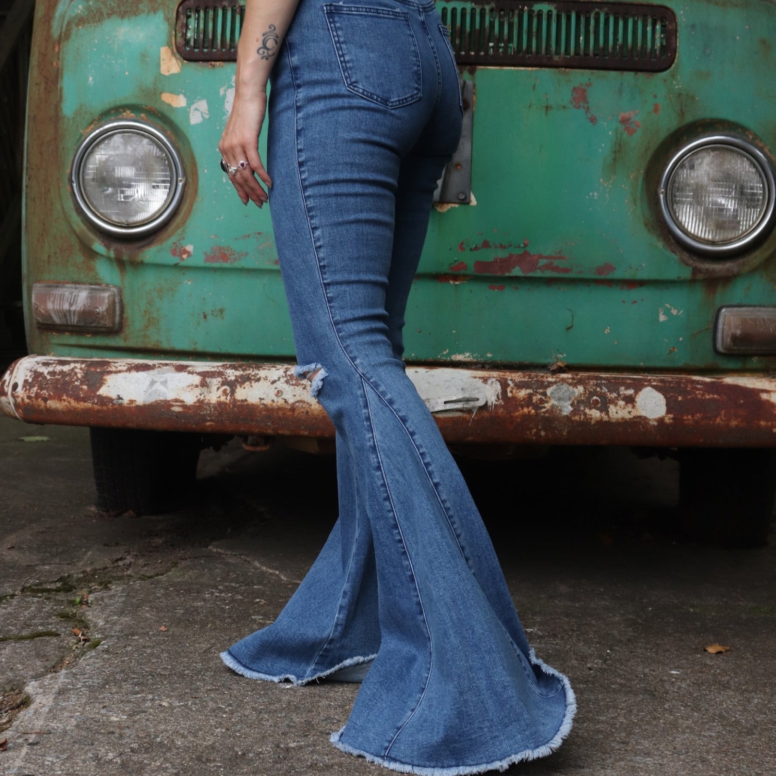 A woman wearing the Western Midtone Ripped and Fringed Stretchy Flared Jeans with a red, orange, and brown top all in front of a vintage Volkswagen bus.