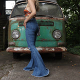 A woman wearing the Western Midtone Ripped and Fringed Stretchy Flared Jeans with a red, orange, and brown top all in front of a vintage Volkswagen bus.