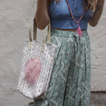 A woman wearing blue pants and a halter top with the African Off White and Tan Mud Cloth Tote with Pink Faux Fur on her shoulder all in front of a white wall.