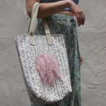A woman wearing blue pants and a halter top with the African Off White and Tan Mud Cloth Tote with Pink Faux Fur on her shoulder all in front of a white wall.