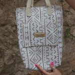 Someone holding the African Off White and Tan Mud Cloth Tote with Pink Faux Fur to show off its back pocket in front of a sandy stone wall.