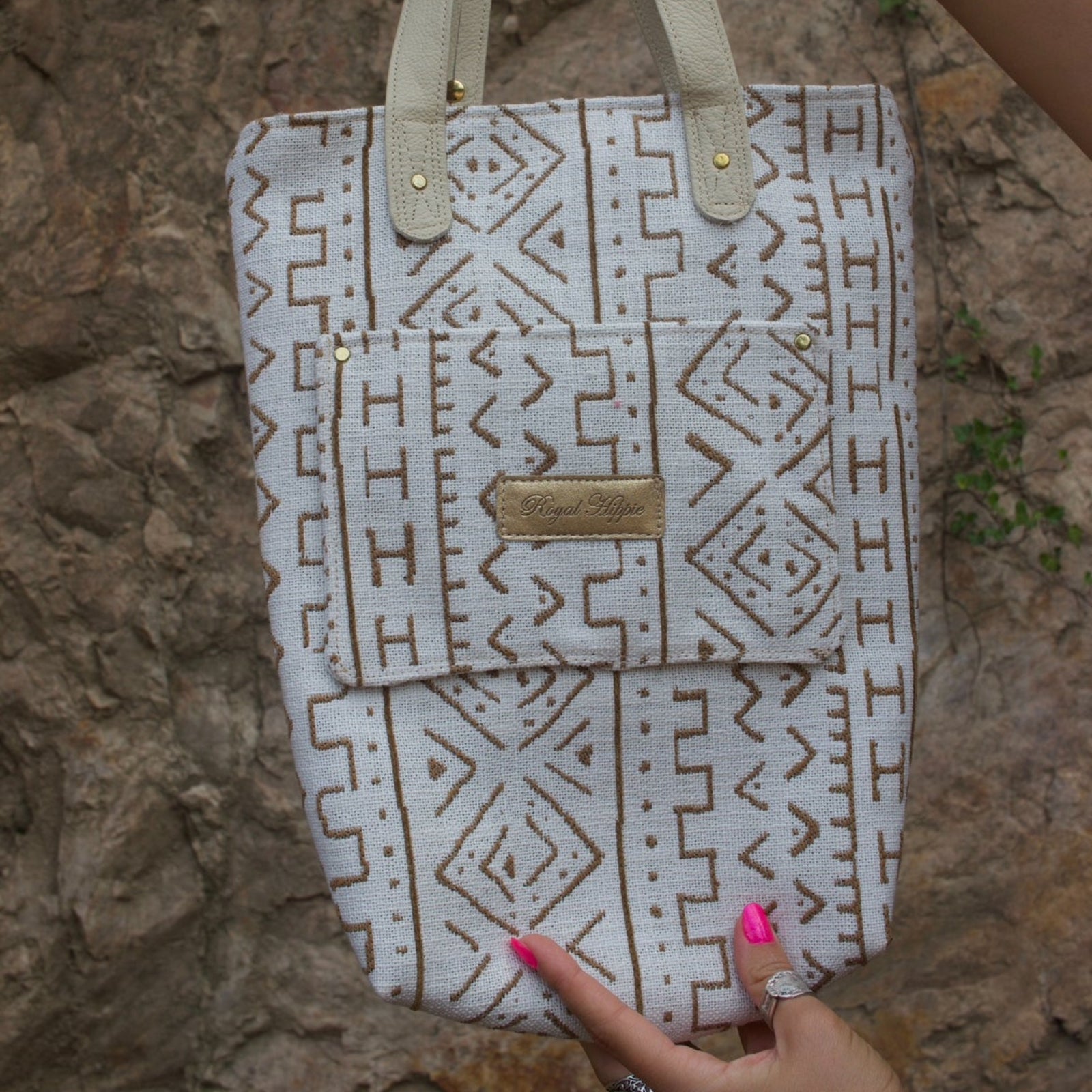Someone holding the African Off White and Tan Mud Cloth Tote with Pink Faux Fur to show off its back pocket in front of a sandy stone wall.