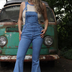 A woman wearing the light denim Bell Bottom Overalls with a cream tank all in front of a vintage Volkswagen bus.