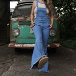 A woman wearing the light denim Bell Bottom Overalls with a cream tank all in front of a vintage Volkswagen bus.
