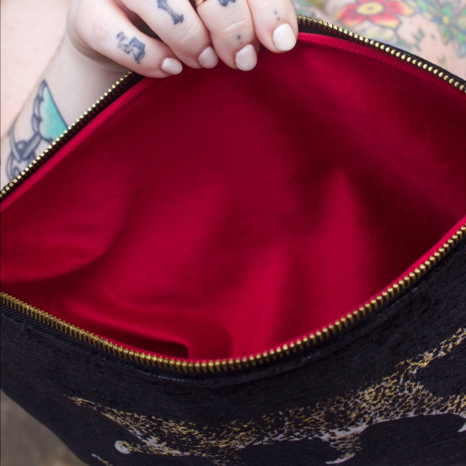 A woman holding the Black Velvet Leopard Traveller Large Pouch open to show off the red velvet lining.