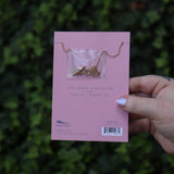 Someone holding the Leo 14k Gold Dipped Nickel-Free Zodiac Necklace on its card in front of greenery showing off the back.