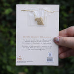 Someone holding the marigold 14k Gold Dipped Nickel-Free Birth Month Flower Necklace in front of greenery showing off the back.
