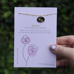 Someone holding the violet 14k Gold Dipped Nickel-Free Birth Month Flower Necklace in front of greenery.