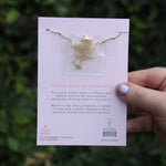 Someone holding the cherry blossom 14k Gold Dipped Nickel-Free Birth Month Flower Necklace in front of greenery showing off the back.