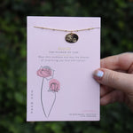 Someone holding the rose 14k Gold Dipped Nickel-Free Birth Month Flower Necklace in front of greenery.