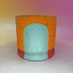 The Phoebe Multicolored Portal Stoneware 5 in. Planter on a pink and yellow background.