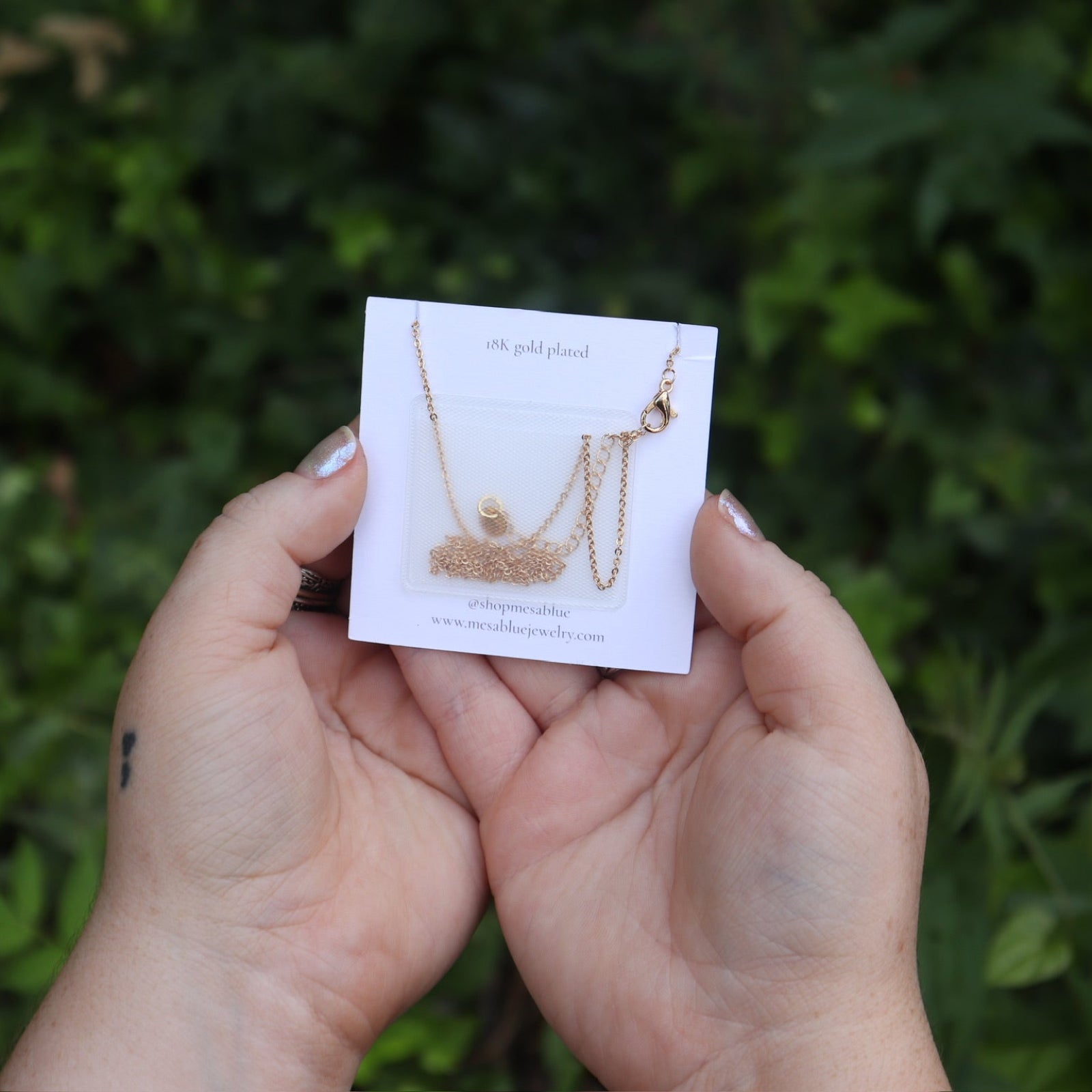 Someone holding the Tiny Turquoise Moon Necklace in front of greener showing off the back.