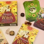 The Lammas Oracle Card Deck and its contents surrounded by tumbled crystals on a pink and yellow background.
